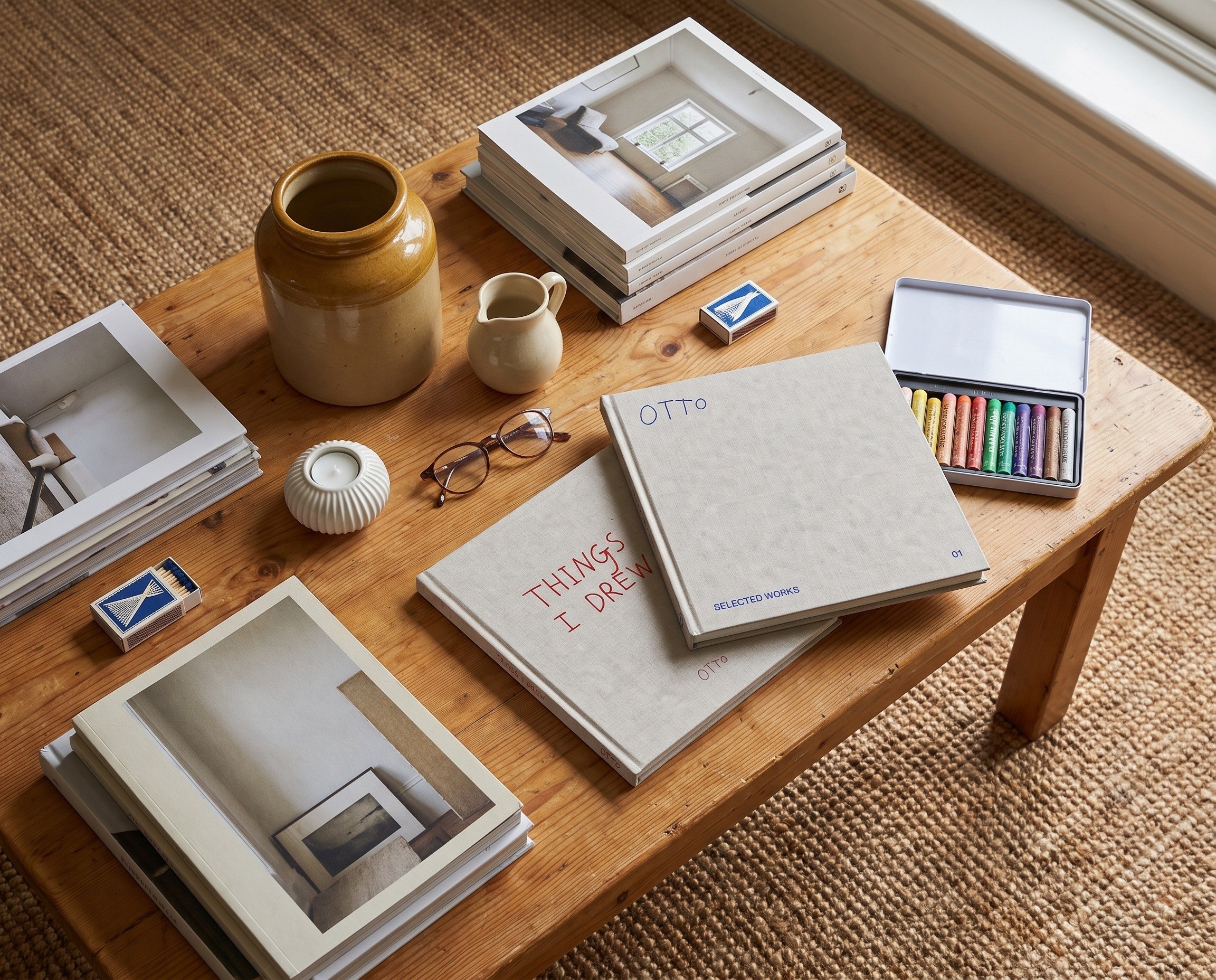 Two EVERYTHING I DREW books on a pine coffee table among art books, stoneware and a tin of oil pastels