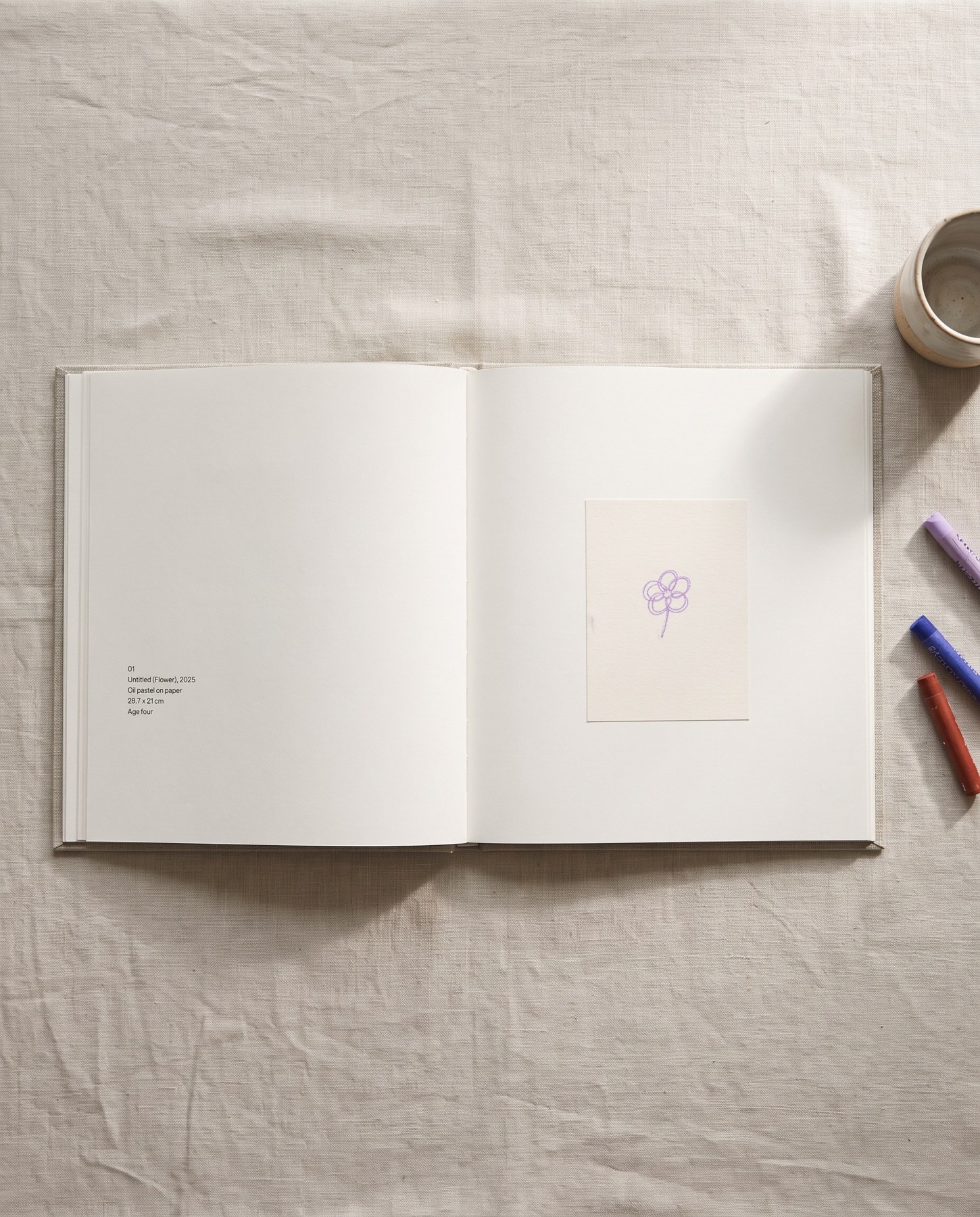 The book open on a linen tablecloth: a single lilac flower on the right-hand page